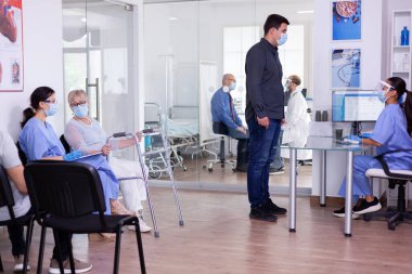 Hastanede beklerken Coronavirus 'a karşı maske takan genç bir adam.