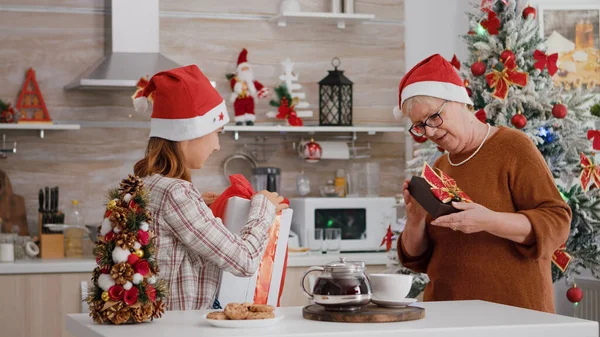 Família feliz vestindo chapéu de Papai Noel surpreendendo uns aos outros com presente de presente de Natal wrapper — Fotografia de Stock