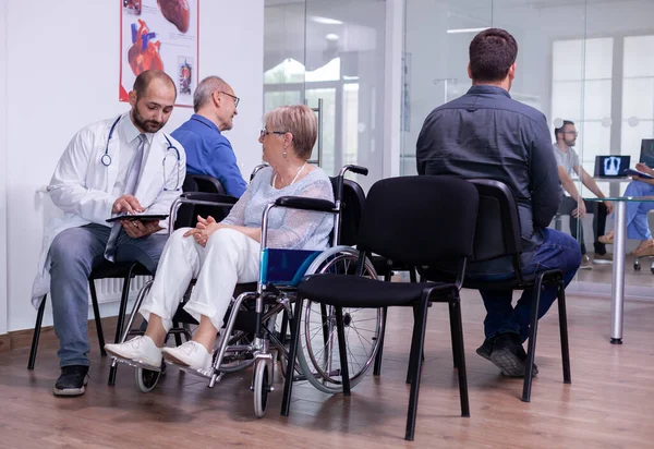 Krankenhausarzt im weißen Kittel kommuniziert mit Seniorin im Rollstuhl — Stockfoto