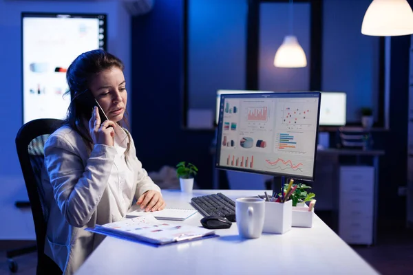 Zakenvrouw spreekt op smartphone met haar teamgenoot tijdens het werken op de computer — Stockfoto