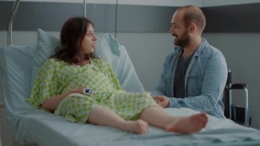 Hamileliği olan beyaz adam hastane koğuşunda bir adamla oturuyor.