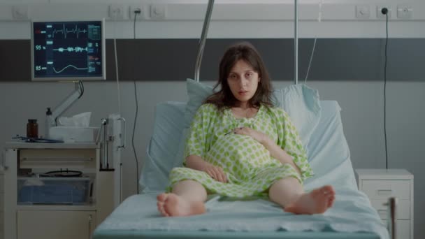 Portrait of pregnant person sitting in hospital ward bed — Stock Video