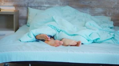 Battaniyenin altında erkek ve kadın ayakları görünüyor.