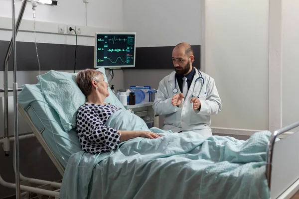 Läkare sitter bredvid så sjuk sjuk seniorpatient ligger i sängen — Stockfoto