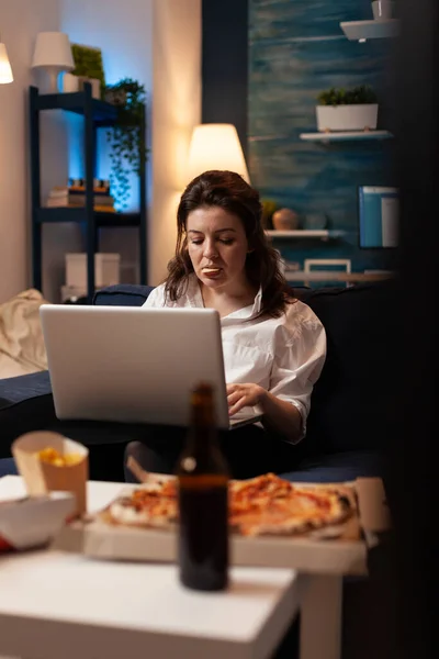 Vrouw eten smakelijke snack werken op laptop computer tijdens het kijken naar documentaire film — Stockfoto