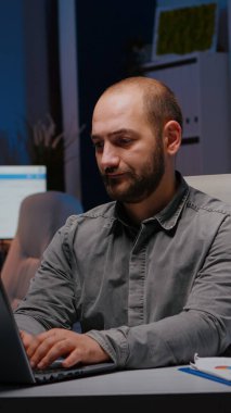 Masada oturan dizüstü bilgisayarında mali istatistikler yazan aşırı çalışan iş adamı.