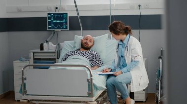 Hasta adam yatakta oksijen tüpüyle dinleniyor. Doktorla konuşuyor. Hastalık belirtilerini açıklıyor.