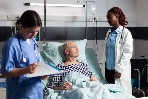 African doctor in hospital room discussing with sick senior man