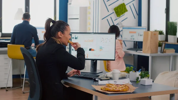 Gestionnaire exécutif manger une pizza savoureuse tout en tapant des statistiques financières au bureau sur le lieu de travail — Photo