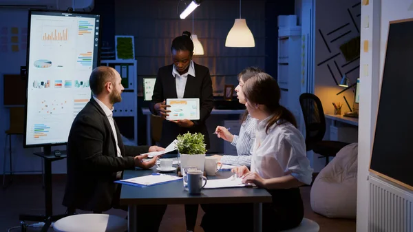 Exhausto afroamericano adicto al trabajo mostrando gráficos financieros usando tabletas trabajando en exceso en la oficina de la compañía — Foto de Stock