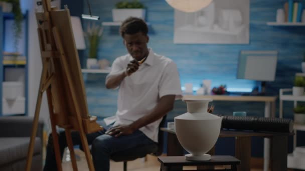 Yaratıcı proje için siyah genç adam vazo çiziyor. — Stok video