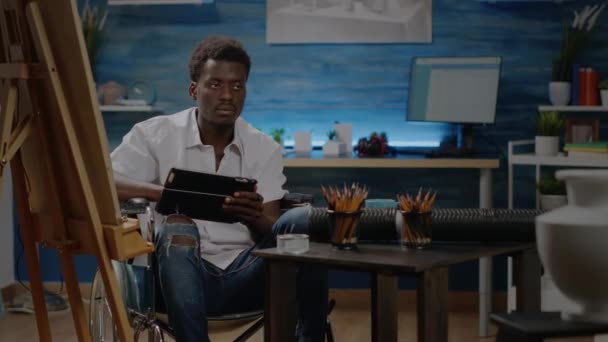 Zwarte kunstenaar zit in een rolstoel met behulp van digitale tablet — Stockvideo