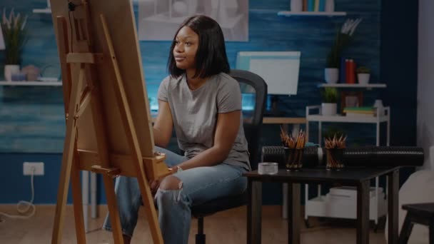 Μαύρη καλλιτέχνης γυναίκα κάθεται στο στούντιο με καμβά και καβαλέτο — Αρχείο Βίντεο