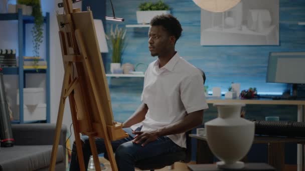 Αφροαμερικάνος που κάθεται στο στούντιο με ζωγραφιές — Αρχείο Βίντεο