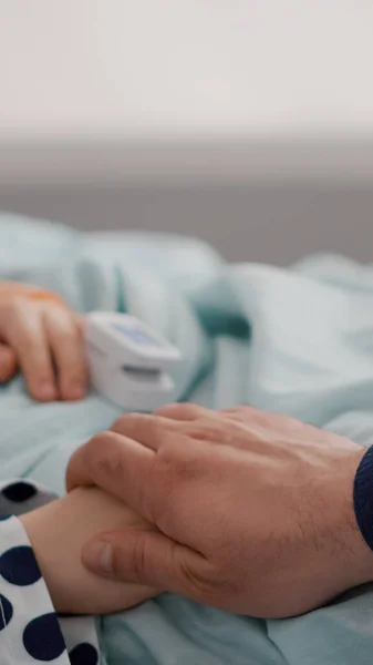 Closeup of sick child resting in bed with oximeter on finger monitoring heartbeat pulse