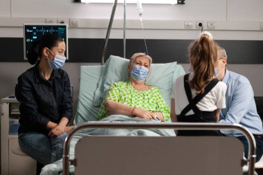 Hasta büyükanneyi ziyaret ederken Covid19 'a karşı koruyucu maske takan aile.