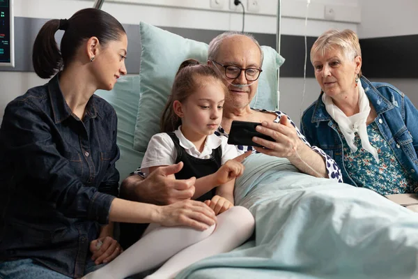 Famiglia allegra visita nonno anziano nel reparto ospedaliero durante il recupero clinico — Foto Stock