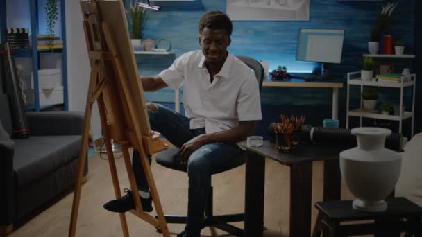 Zwarte kunstenaar met potlood en wit doek op ezel voor ontwerp — Stockvideo
