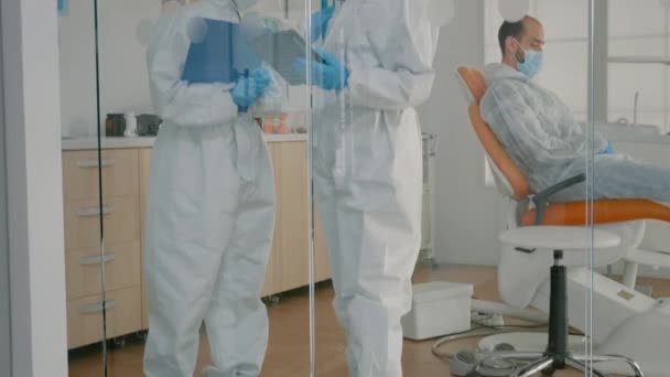 Equipo de dentistas con trajes ppe que sostienen la tableta para consulta de dientes — Vídeo de stock