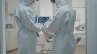 Diş hekimlerinden oluşan bir ekip röntgene bakarken takım elbise giyiyor.