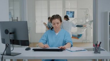Dişçi hemşiresi masada oturup bilgisayar klavyesinde yazıyor.