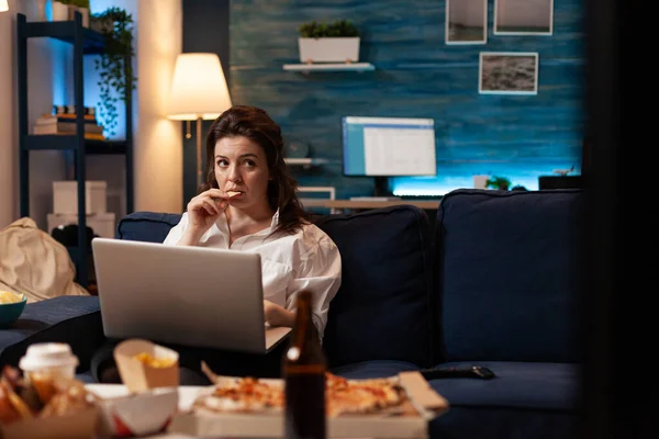 Mujer comiendo sabroso bocadillo de trabajo en el ordenador portátil mientras ve la película documental — Foto de Stock
