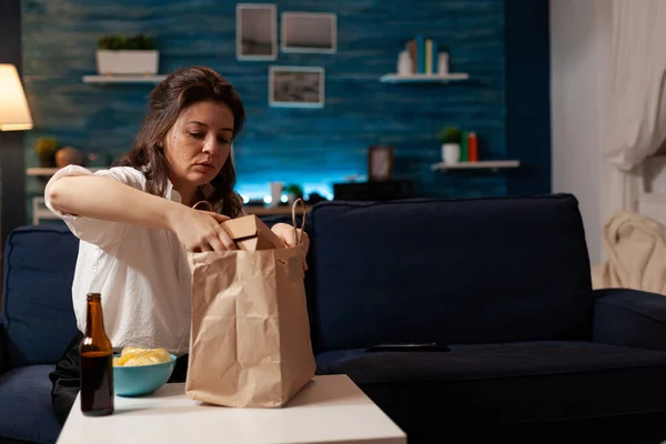 Fröhlich lächelnde Frau beim Auspacken von Fast-Food-Essenslieferung auf Sofa sitzend während Junk-Food-Lieferung nach Hause — Stockfoto