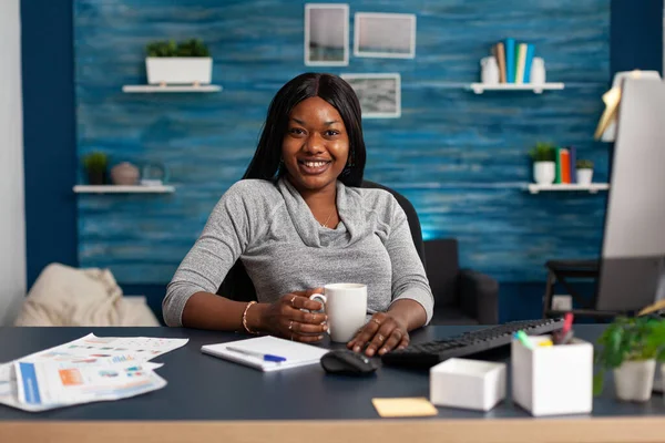 Portrait d'un étudiant noir souriant regardant dans la caméra alors qu'il était assis à la table du bureau dans le salon — Photo