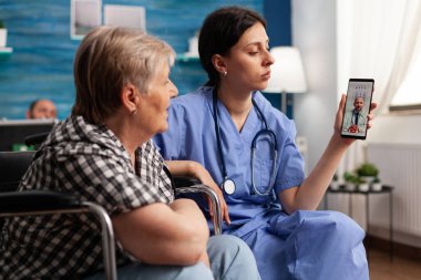 Huzurevi kadın çalışanı. Emekli, engelli, yaşlı bir kadına video çağrısı yapması için yardım ediyor.