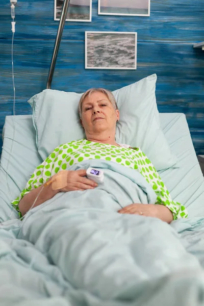 Porträt einer gehbehinderten Rentnerin, die im Krankenhausbett liegt und in die Kamera blickt — Stockfoto