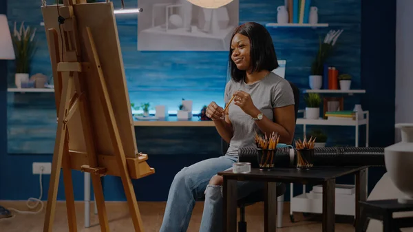 Mulher artista preto sentado no estúdio com tela e cavalete — Fotografia de Stock