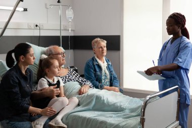 Afrika kökenli Amerikalı hemşire yaşlı yaşlı bir adamla hastalık tedavisini tartışıyor.