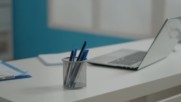 Cierre de bolígrafos y laptop en escritorio blanco en gabinete vacío — Vídeo de stock
