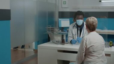 Yaşlı bir hastaya danışırken yüz maskesi takan genç doktor.