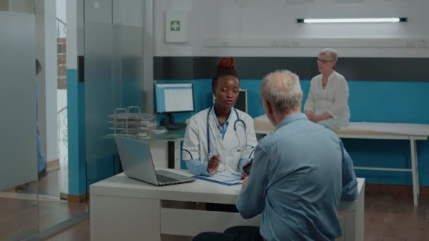 Medic bespreken gezondheidszorg behandeling met oudere man — Stockvideo