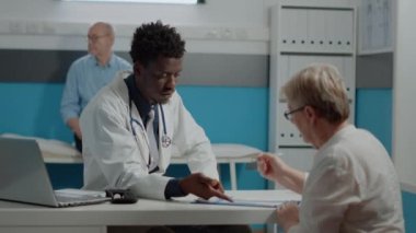 Genç doktor eski hastaya imza için dosya gösteriyor