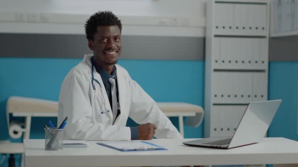 Portret afrykańskiego lekarza siedzącego przy białym biurku — Wideo stockowe