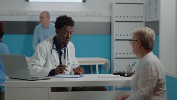 Médico afro-americano escrevendo check-up no notebook — Vídeo de Stock