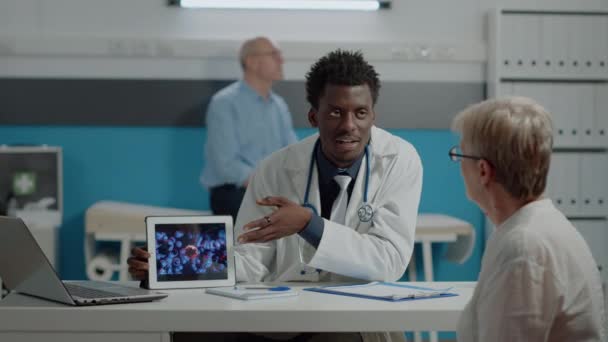 Tânăr medic care analizează animația virusului pe tabletă cu o femeie bătrână — Videoclip de stoc