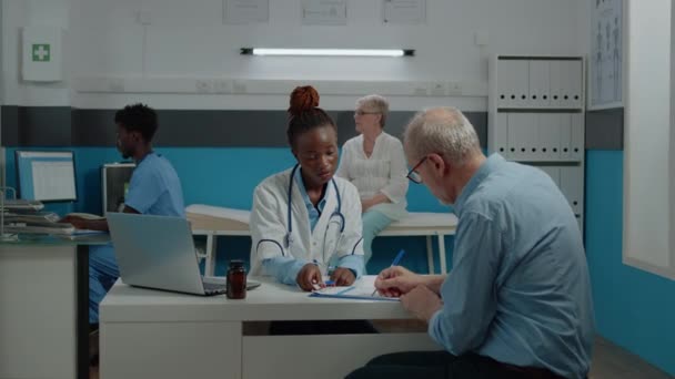 Läkare diskuterar med seniorsjuk patient på vårdcentralen — Stockvideo