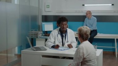 Afrikalı Amerikalı doktor yaşlı bir kadına danışıyor.