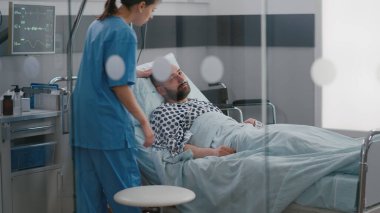 Hasta adam yatakta dinleniyor, nazal oygen tüp takıyor. Hastalık muayenesi için doktor bekliyor.