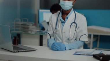 Afro-Amerikan etnik kökenli bir doktor dizüstü bilgisayarla masada oturuyor.