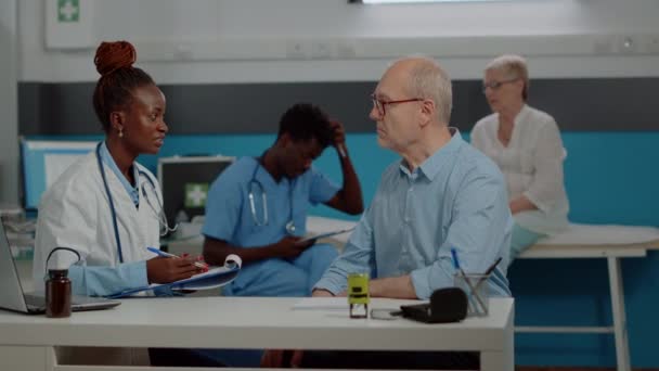 Спеціаліст з охорони здоров'я обговорює зі старим пацієнтом за столом — стокове відео