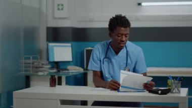 Erkek hemşire masada otururken görüntülü konuşma teknolojisiyle konuşuyor.