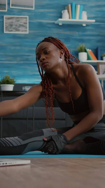 Donna con pelle scura che fa allenamento di pilates in soggiorno allungando i muscoli del corpo — Foto Stock