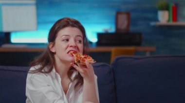 Genç insan televizyon izlerken bir dilim pizza yiyor