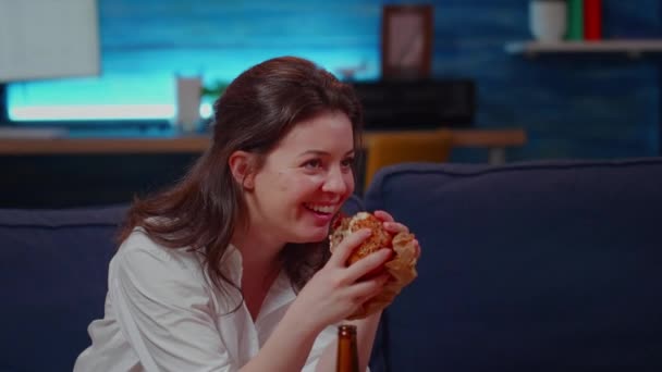 Young person laughing at TV while eating hamburger — Stock Video