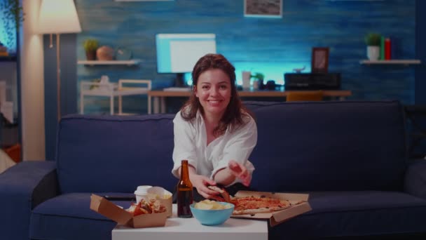 Osoba jedząca kawałek pizzy na kanapie i patrząca w kamerę — Wideo stockowe