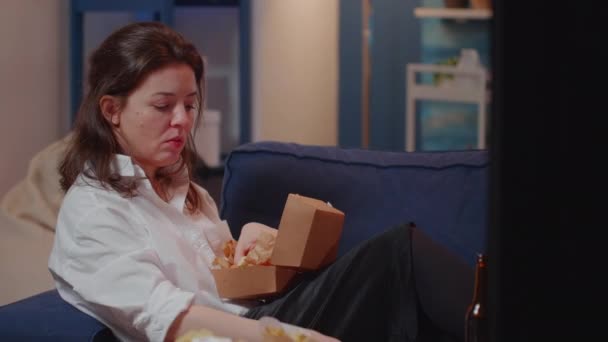 Egy nő csatornát vált, miközben hamburgert eszik. — Stock videók
